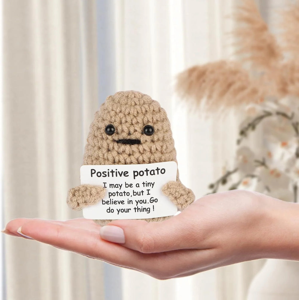 Khaki crochet potato doll with a small card, sitting on an open hand to show its size